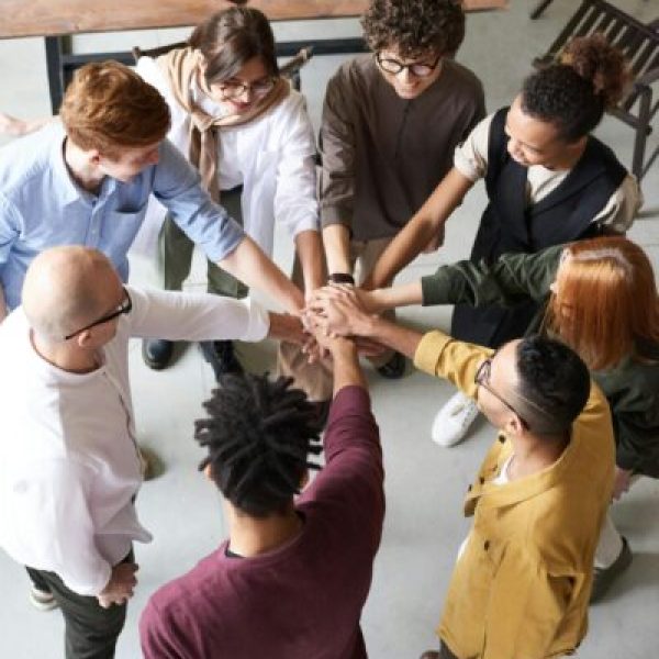 A diverse group of professionals joins hands in a team-building exercise indoors.